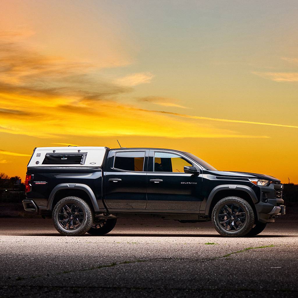 Flated Mid-Short CAP50 Colorado Air Topper truck cap in white, mounted on a black Chevrolet Colorado, photographed at sunset